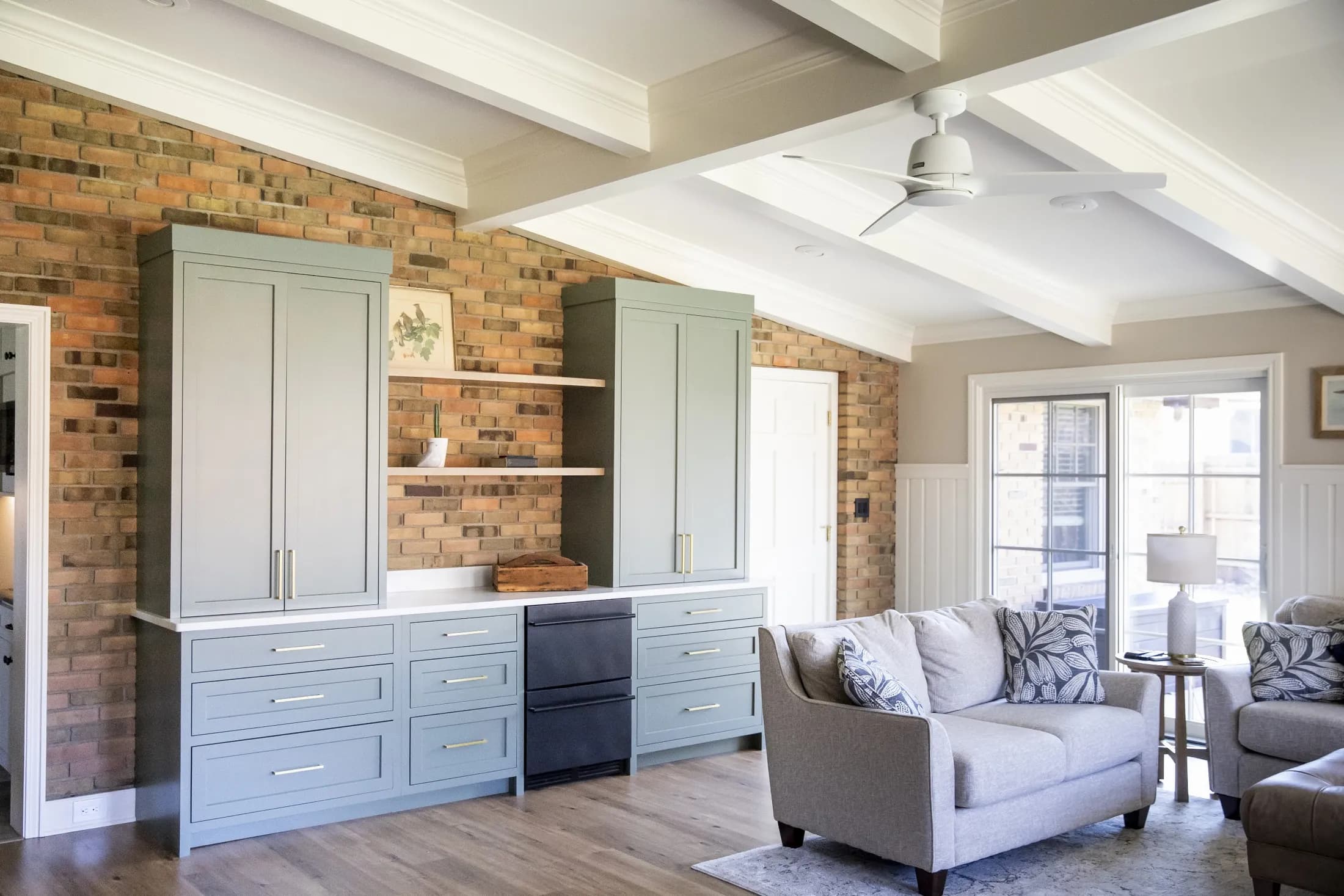 Living room with sage and blue built-in cabinets against brick under a coffered ceiling