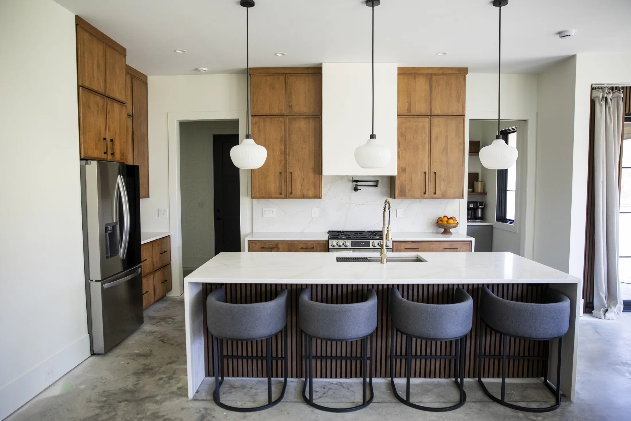 Stained alder cabinets, white waterfall island, gray stools and three pendants