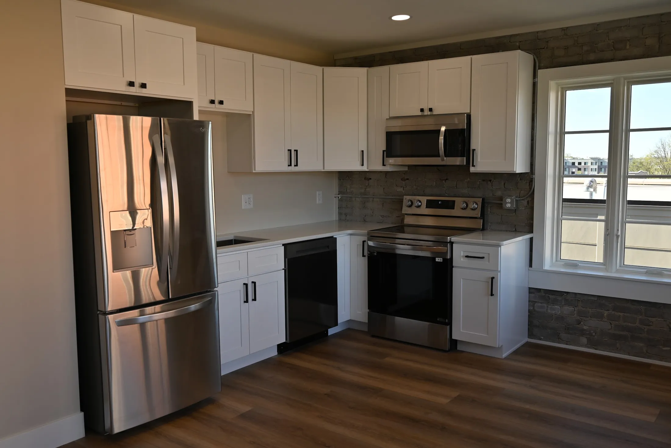 Loft kitchen with white shaker cabinets, exposed brick and tall windows