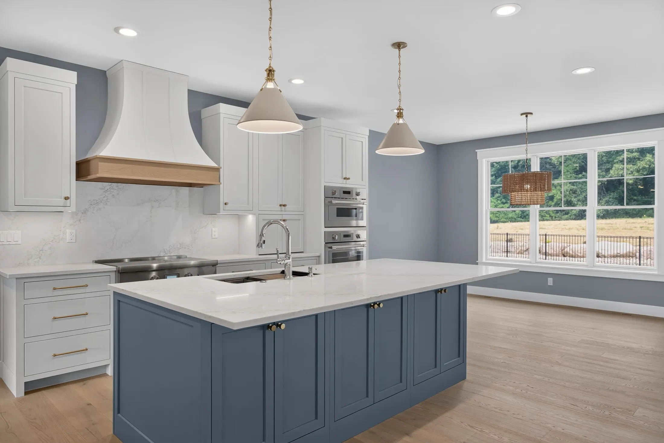 Bright kitchen with blue island, oak-banded white range hood, pendants and double wall ovens